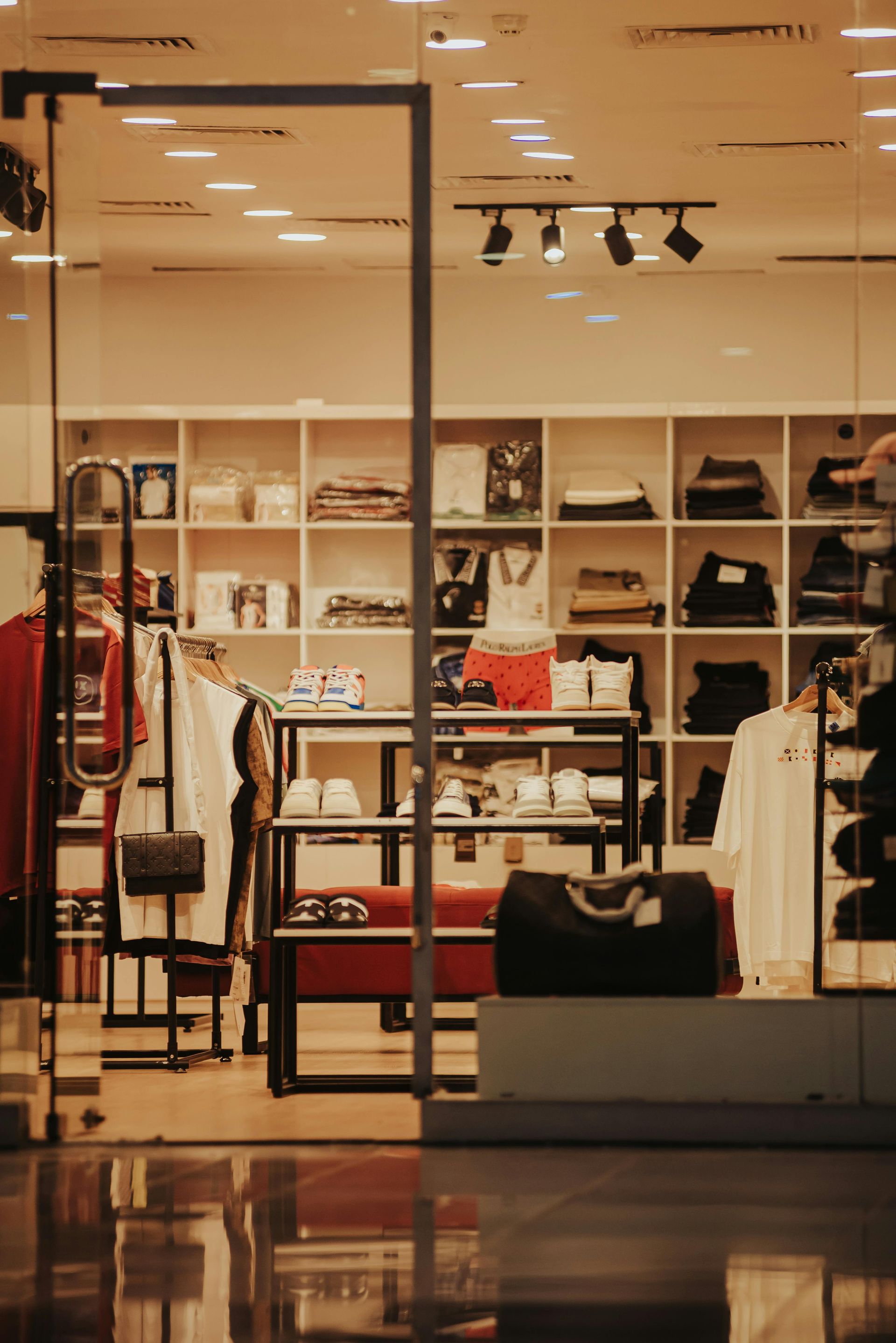 Clothing store interior with shelves of folded clothes and hanging garments under warm lights