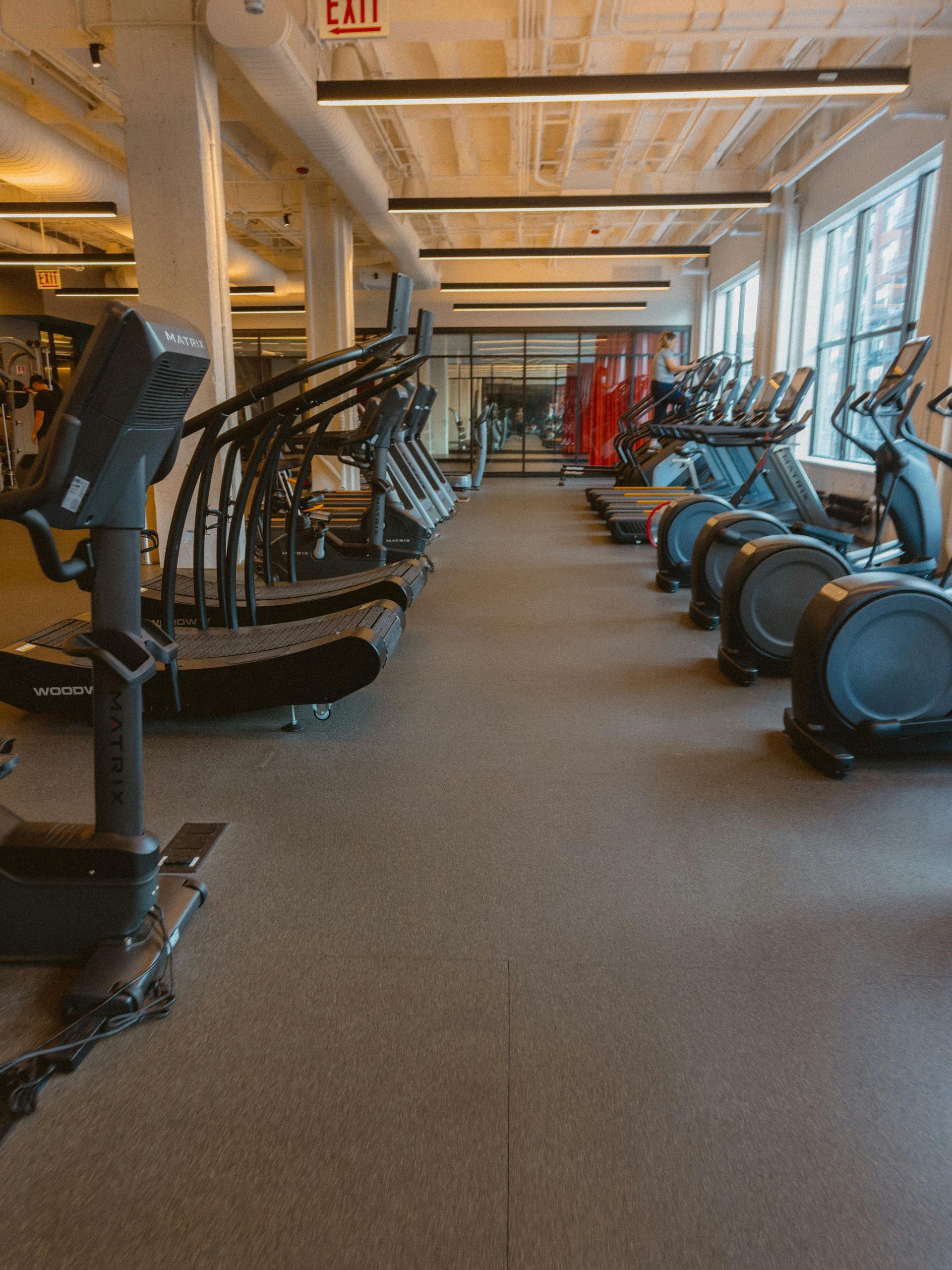 Indoor gym with rows of cardio machines and strength equipment on a carpeted floor.