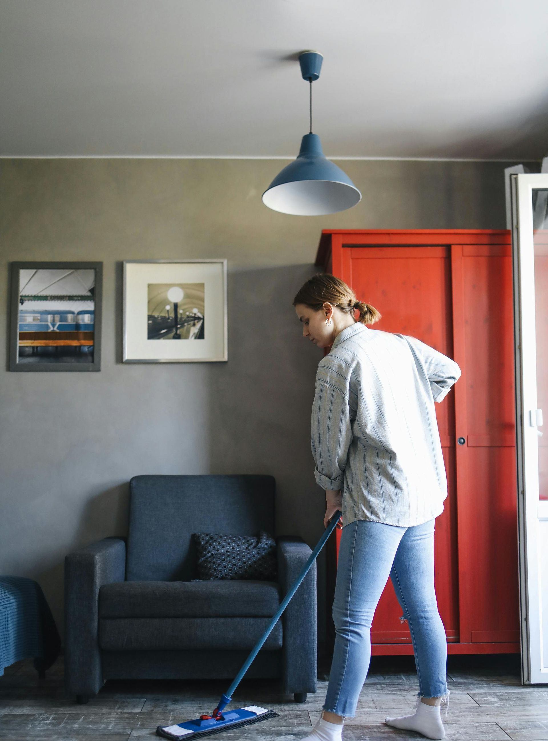 Person vacuuming a living room with gray walls, blue chair, and red cabinet
