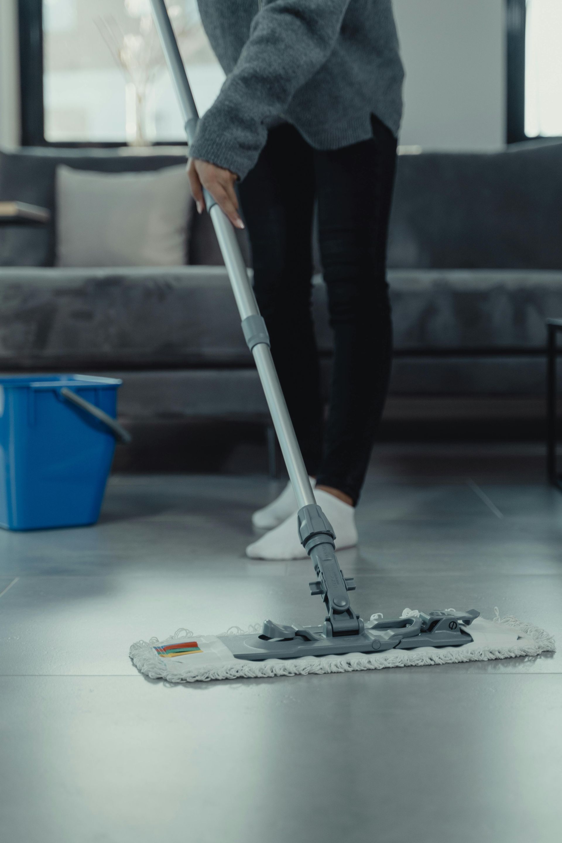 Person mopping a gray floor with a white mop in a modern living room.