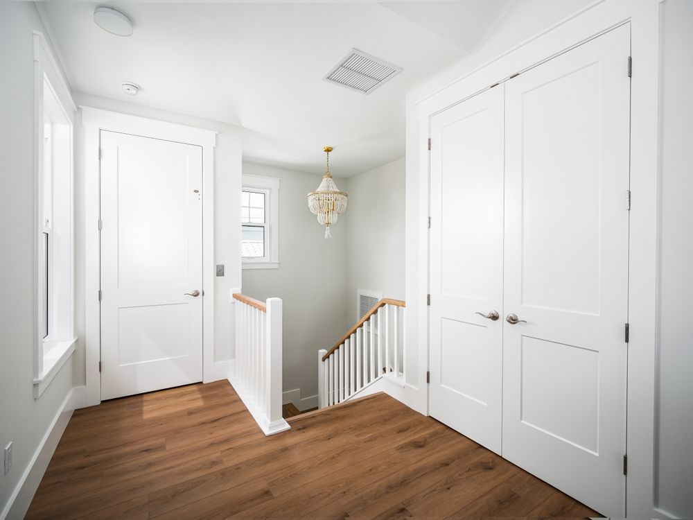 Bright upstairs hallway with white walls, wood floor, double doors, and a stair railing overlooking below