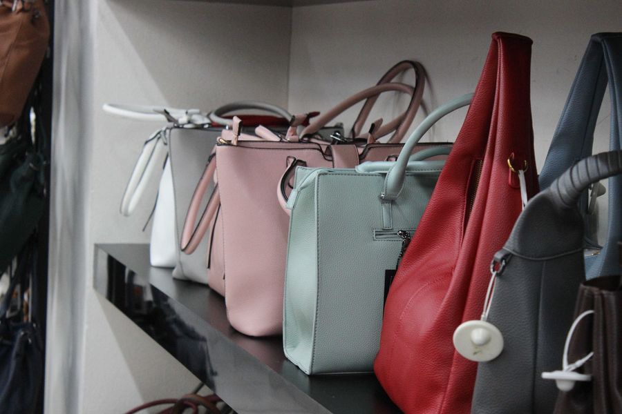 Su uno scaffale è esposta una fila di borse di vari colori, tra cui bianco, grigio, rosa, azzurro, rosso e grigio scuro.