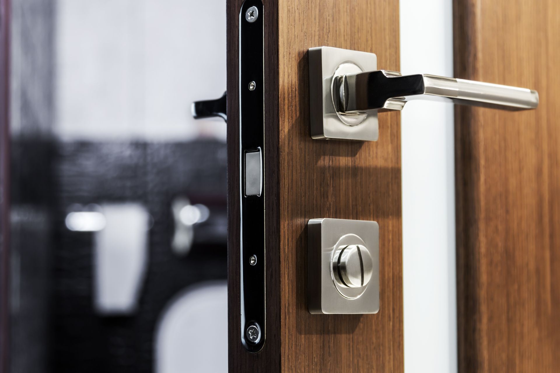 Close-up of a wooden door with a modern silver handle and lock, partially open, showing an interior view.
