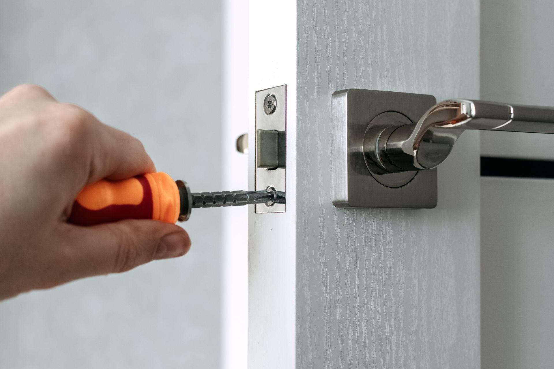 Person using a screwdriver to install a door latch on a white door.