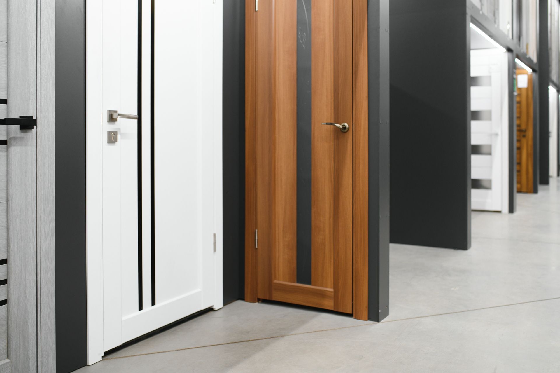 Doors on display in a showroom; white, brown, and black. Grey floor.