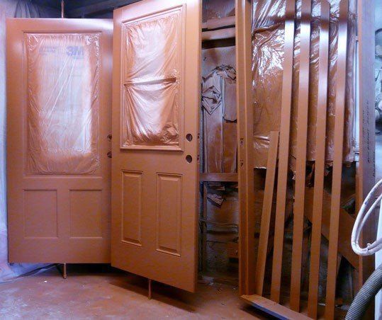 Doors and trim freshly painted orange in a workshop, covered with plastic.
