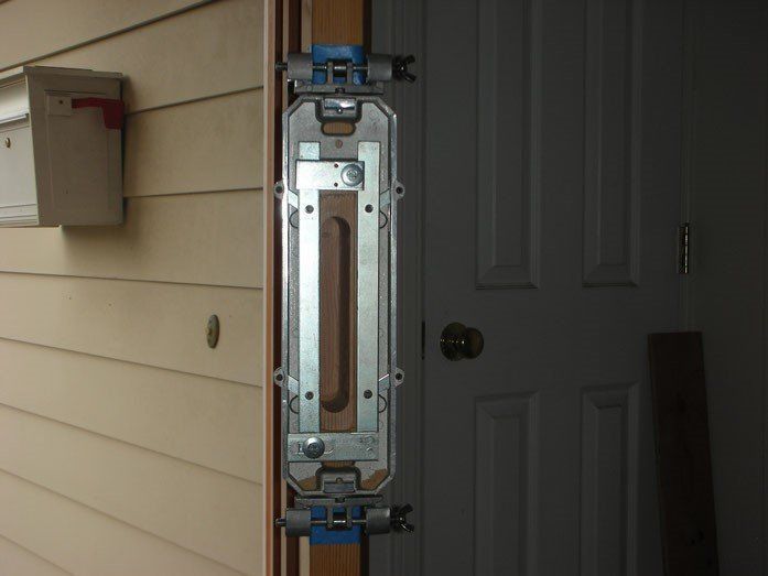 Door frame with a security device installed, beside a white door and mailbox on a light-colored exterior wall.
