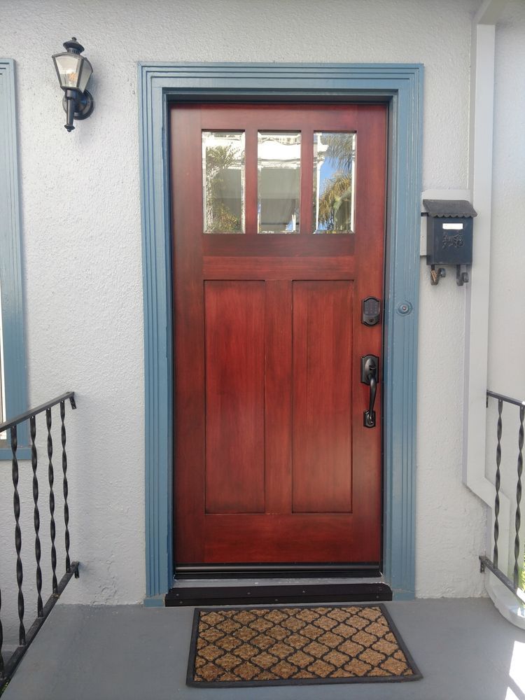Red wooden front door with blue trim, mail slot, and patterned doormat.