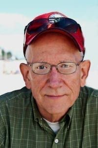 Man wearing glasses and a red cap, looking at the camera outdoors.