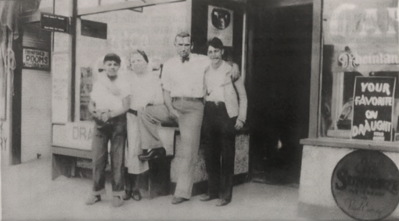 People standing outside a storefront beside a signboard and a display window.