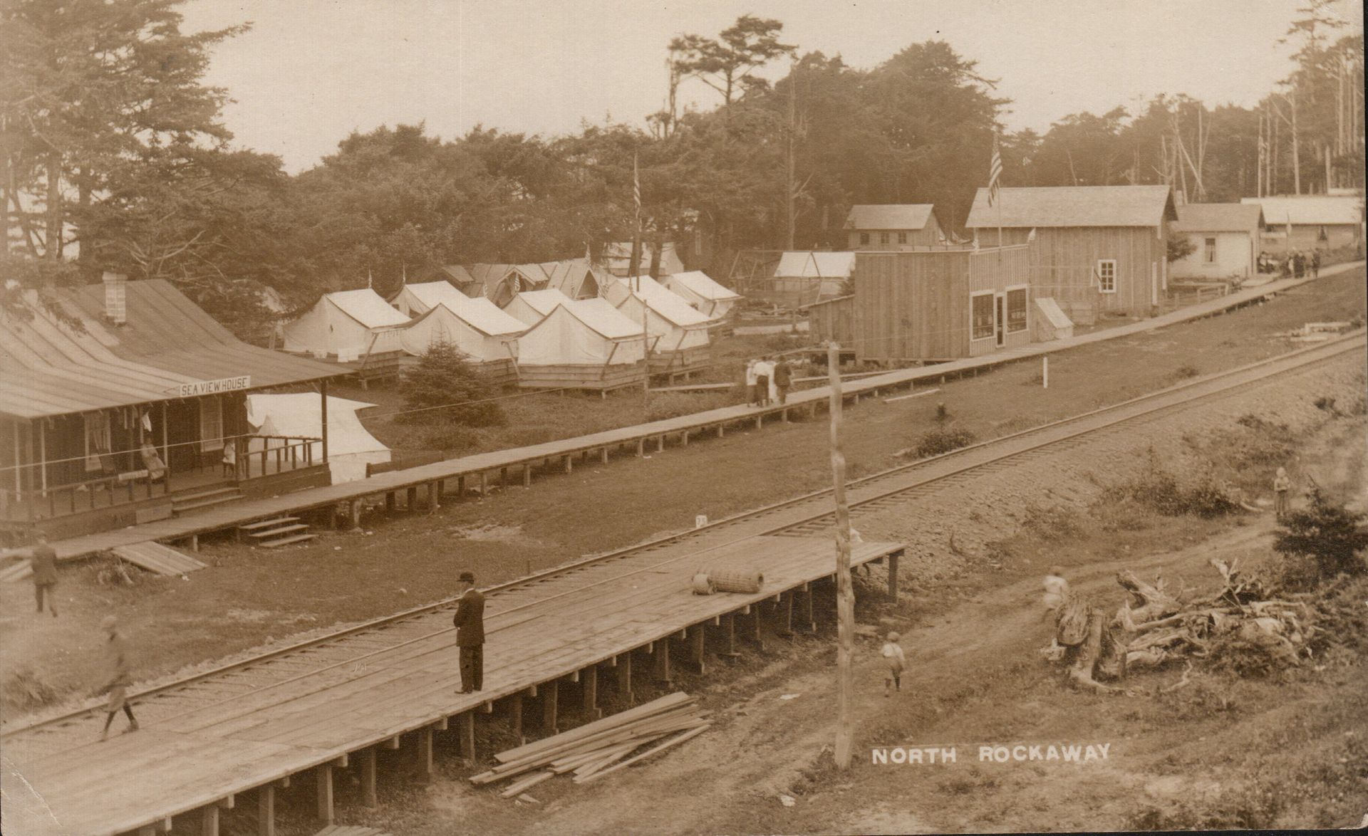 Sepia view of a historic mining camp with tents, wooden buildings, and a rail line