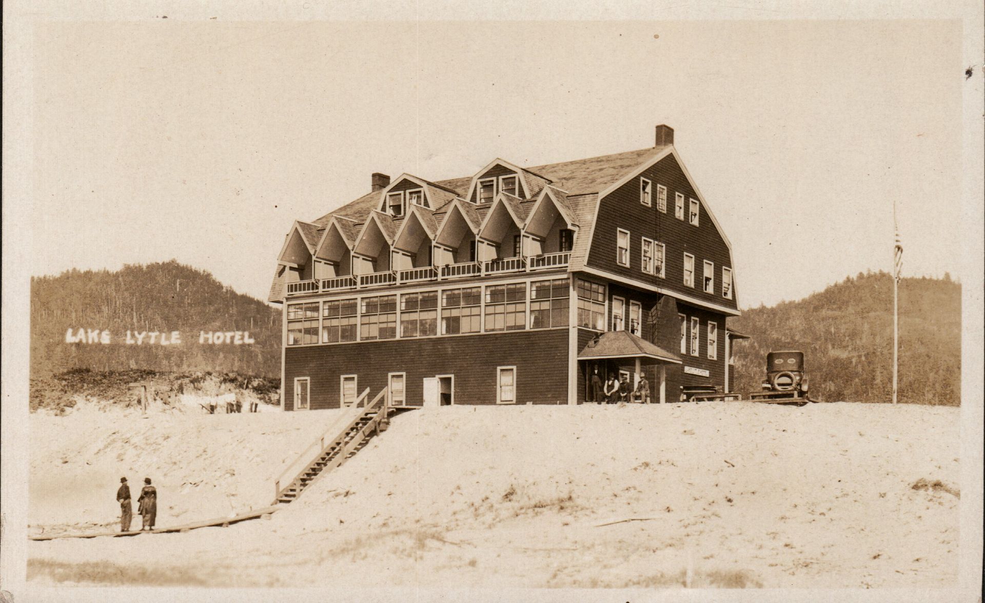Historic hotel building on a sandy hillside with a few people standing in front.