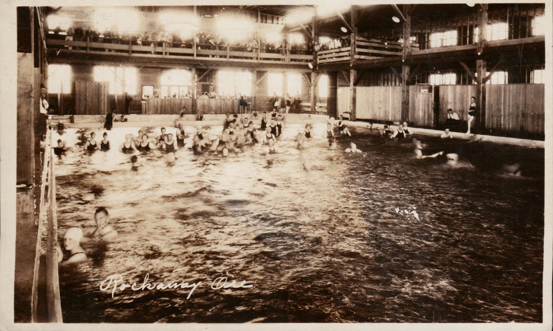 Sepia photo of an indoor swimming pool crowded with swimmers under bright lights