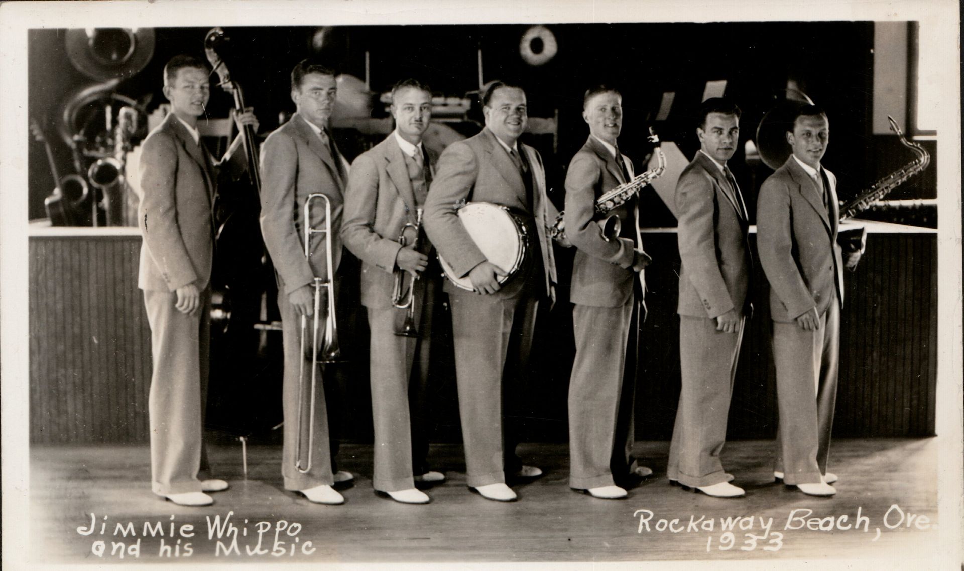 Seven suited men stand in a row on a stage, in a black-and-white photo.