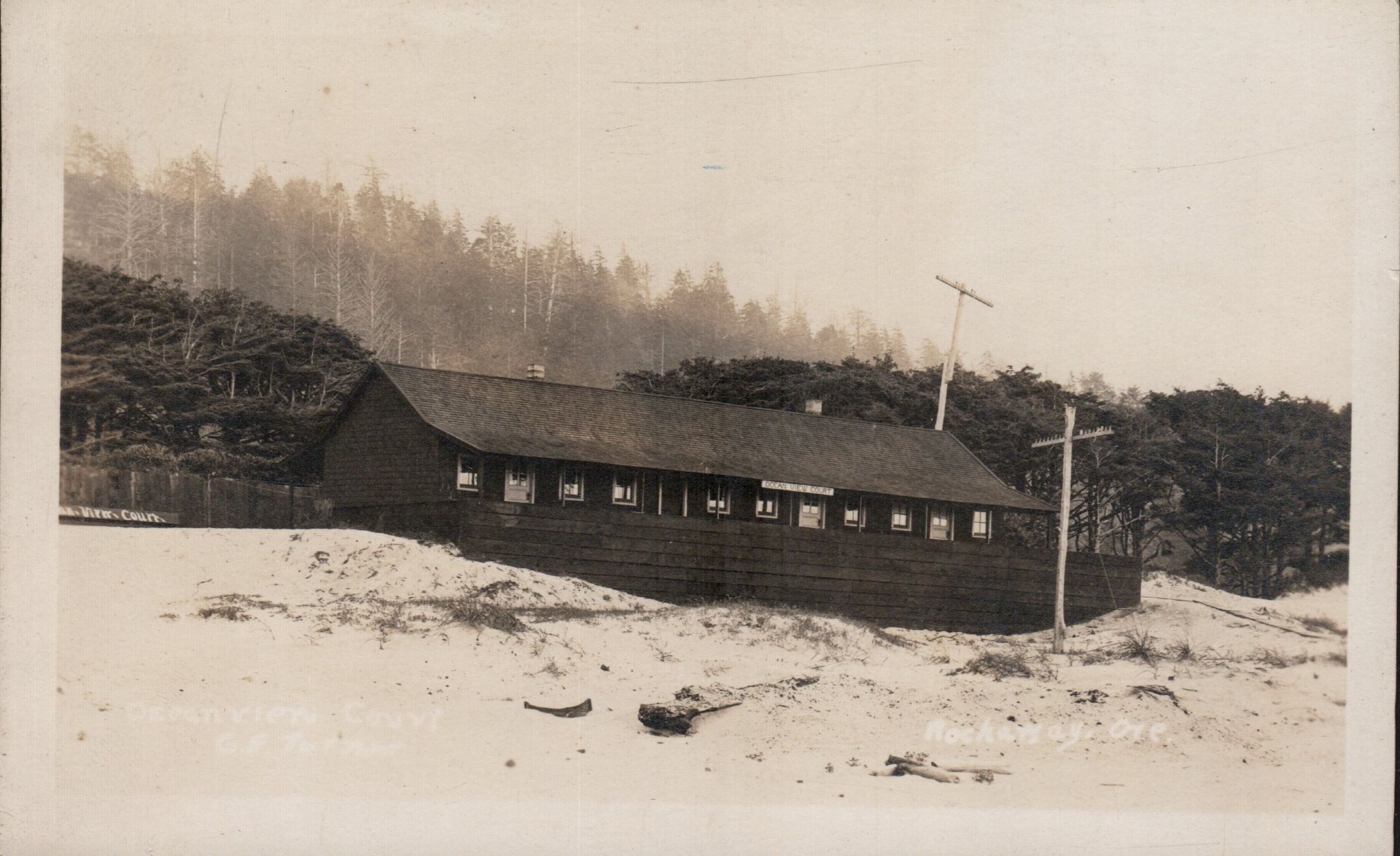 Sandy hillside with a long dark building and trees in the background
