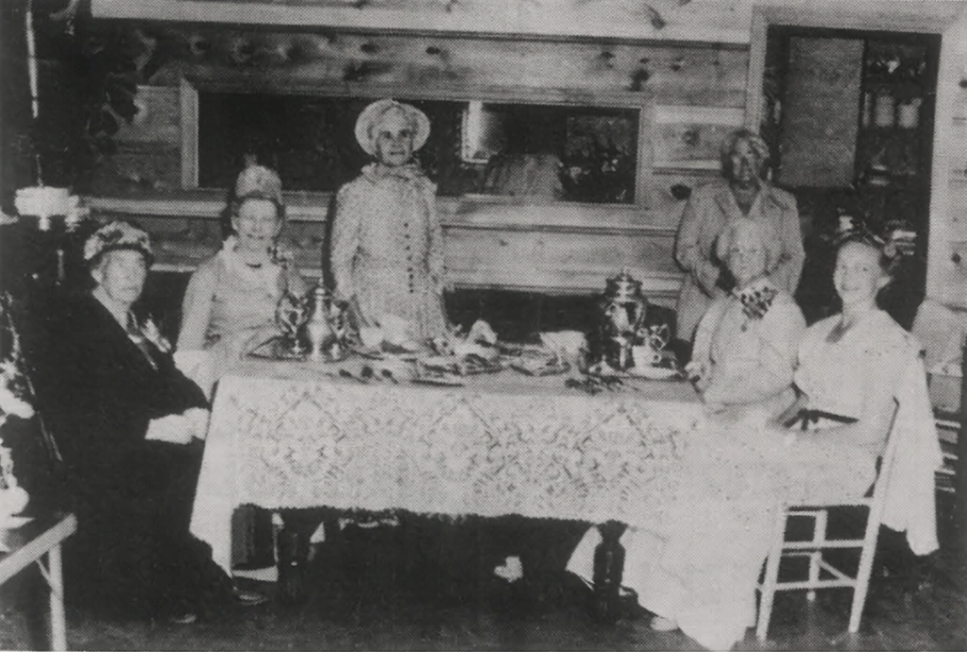 Women seated around a dining table in a vintage black-and-white indoor photograph