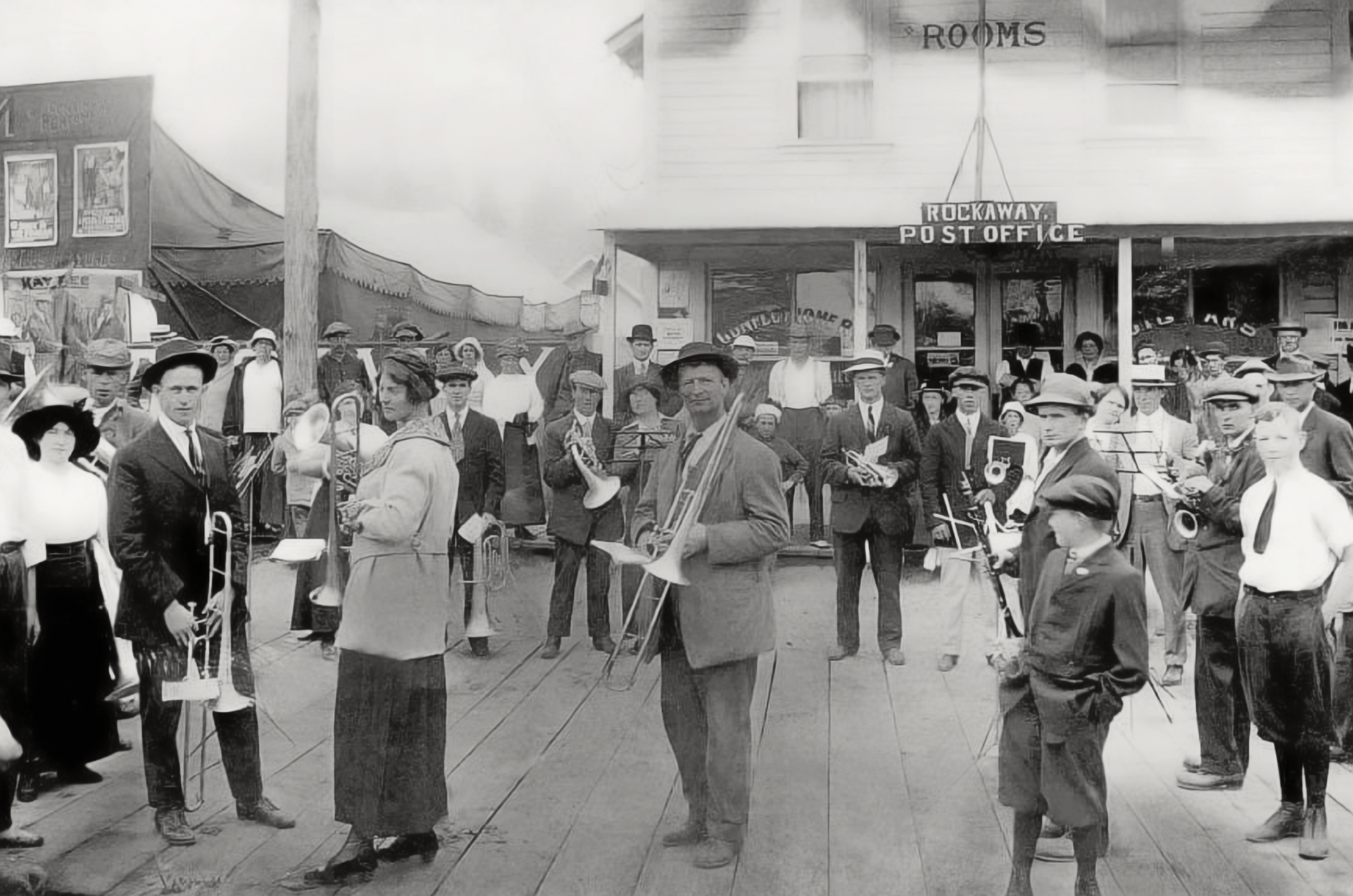 Crowd gathered in a town square for a public event, with people standing around with instruments and buildings in the background.