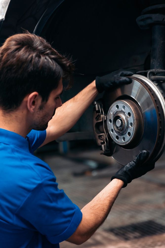 A Man in a Blue Shirt is Fixing a Brake Disc on a Car — A & J Diesel Services in Braitling, NT