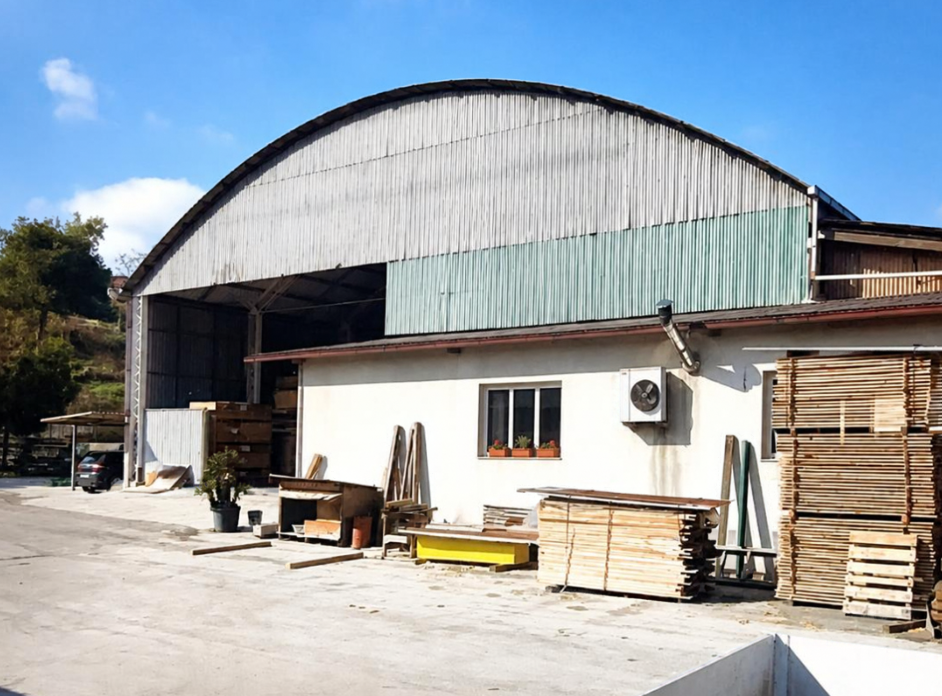 Capannone industriale con legname accatastato e attrezzature in una giornata di sole