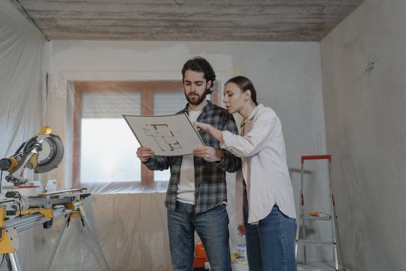 Couple reviewing blueprints in a room under renovation, water damage situation.