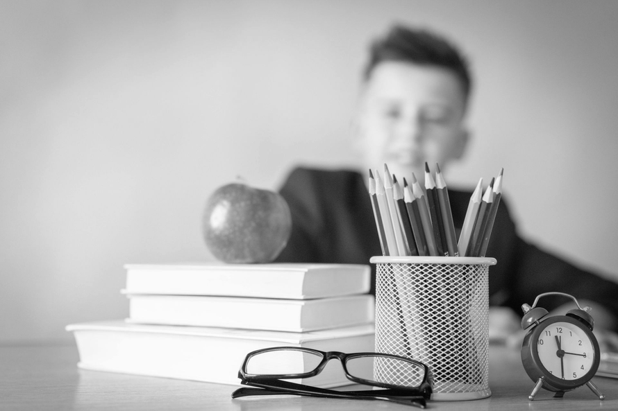 Boy writing in a notebook at a table, pencil in hand. Black and white photo.