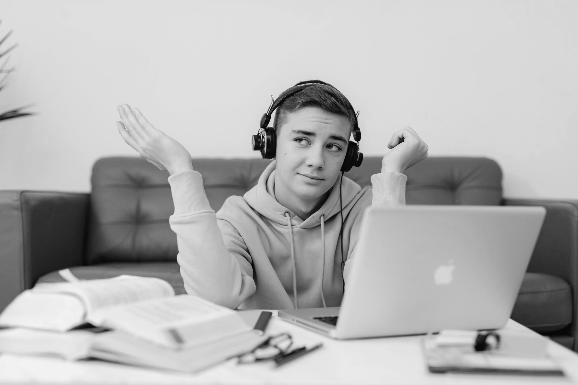Teenager wearing headphones looks perplexed while working on a laptop at a desk.