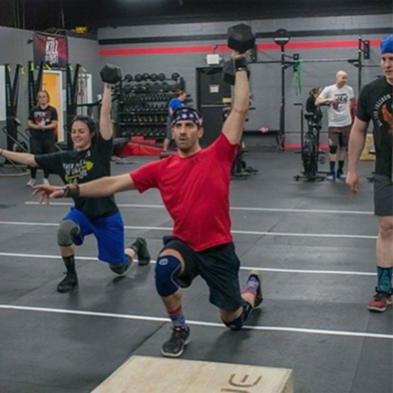 People doing dumbbell lunges in Great Woods CrossFit, a gym in Norton, MA, with a man in a red shirt centered in front.