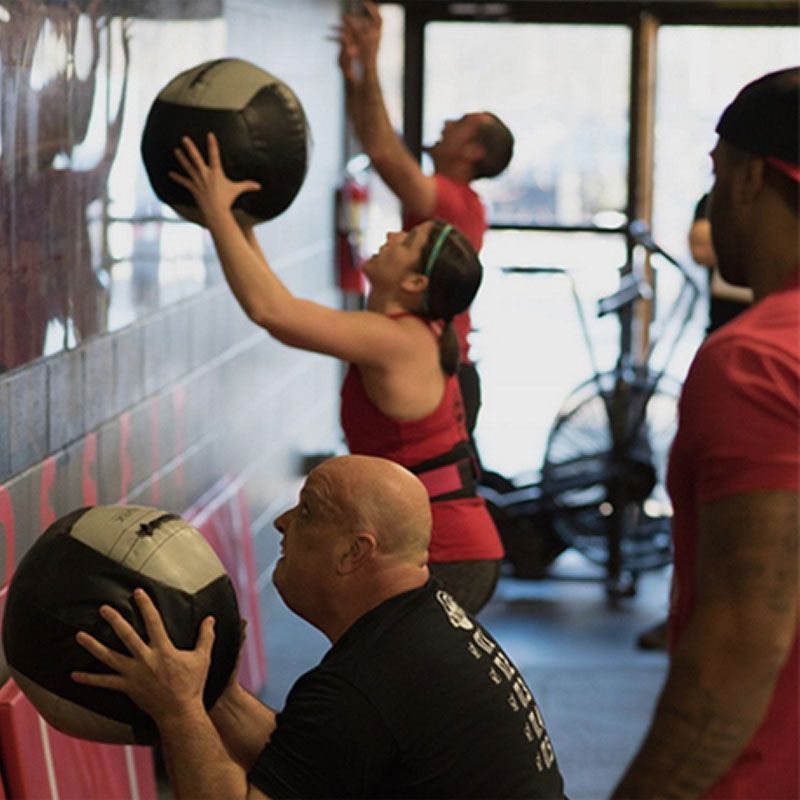 People exercising with medicine balls in Great Woods CrossFit, a gym in Norton, MA, reaching toward a wall target.