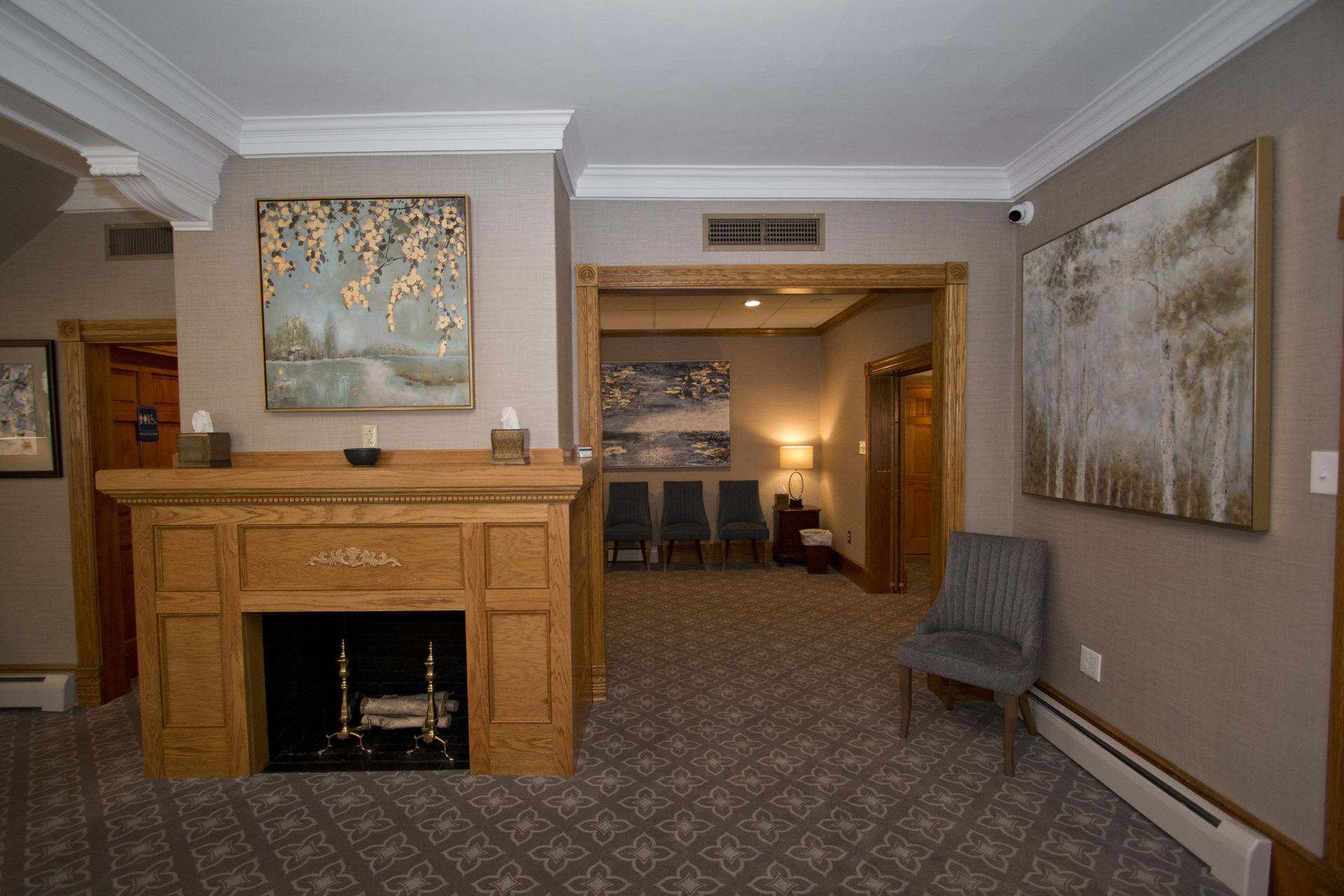Hotel lobby with fireplace, patterned carpet, and framed wall art in beige tones