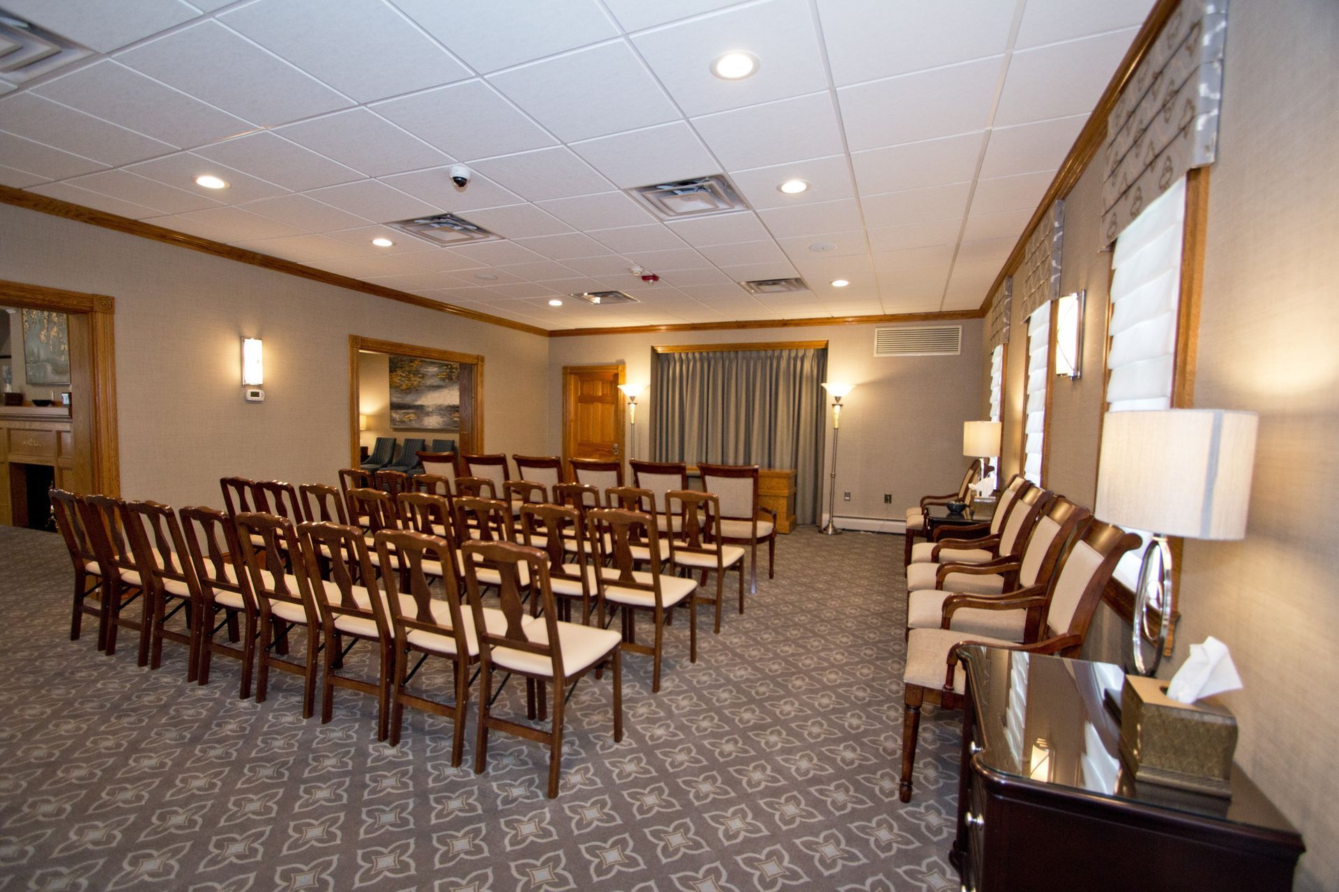 Empty conference room with rows of wooden chairs, carpeted floor, and a podium under recessed ceiling lights