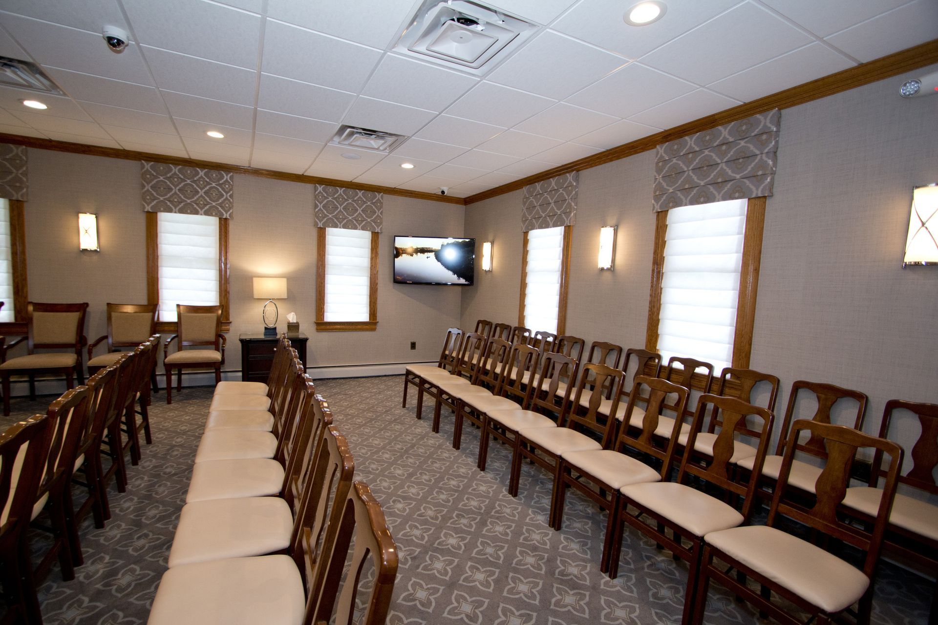 Empty banquet room with rows of wooden chairs and upholstered benches facing the front wall.