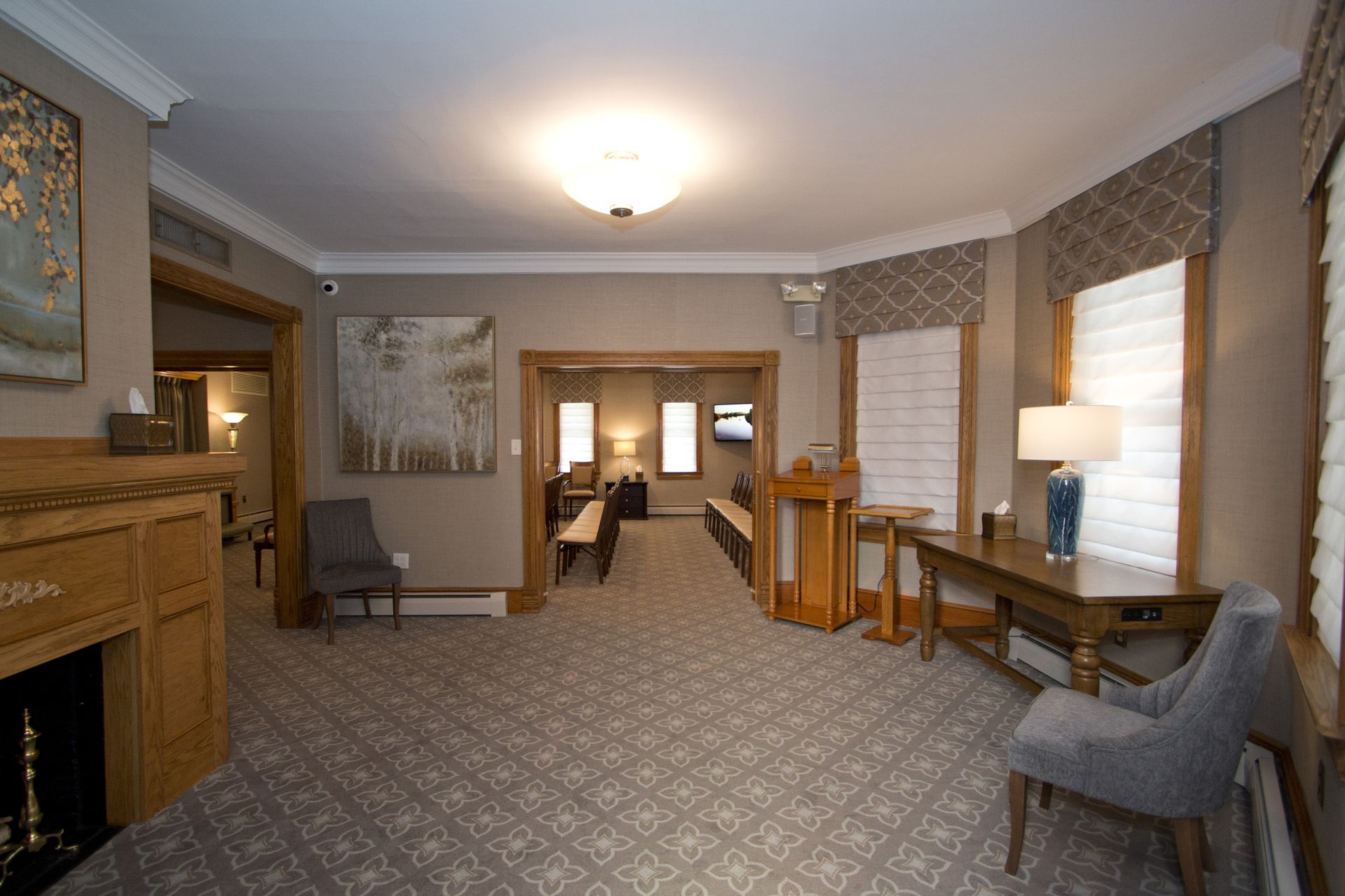 Hotel lobby with patterned carpet, wood furniture, lamps, and windows along the wall