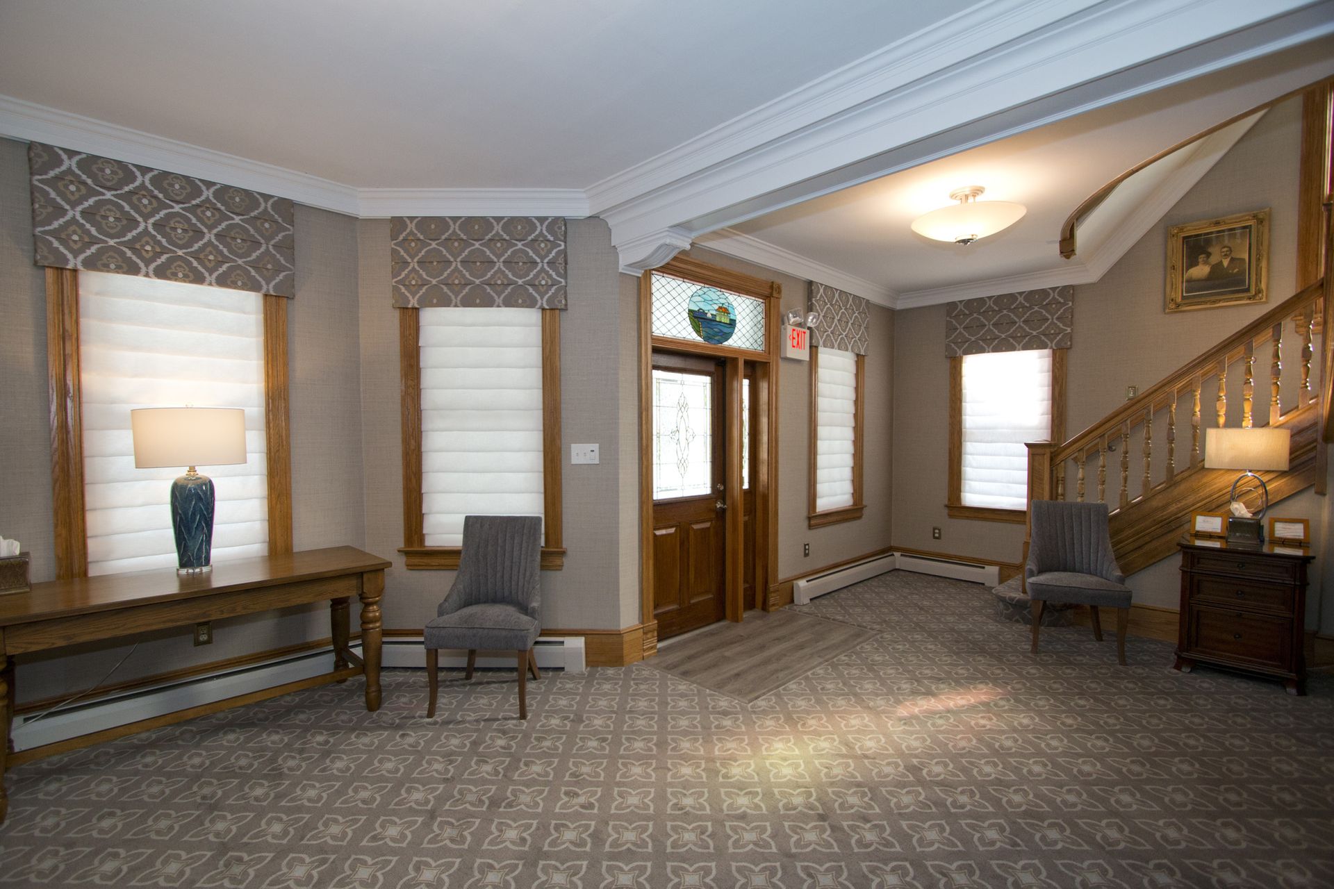 Elegant foyer with patterned carpet, armchairs, console table, lamp, staircase, and front door