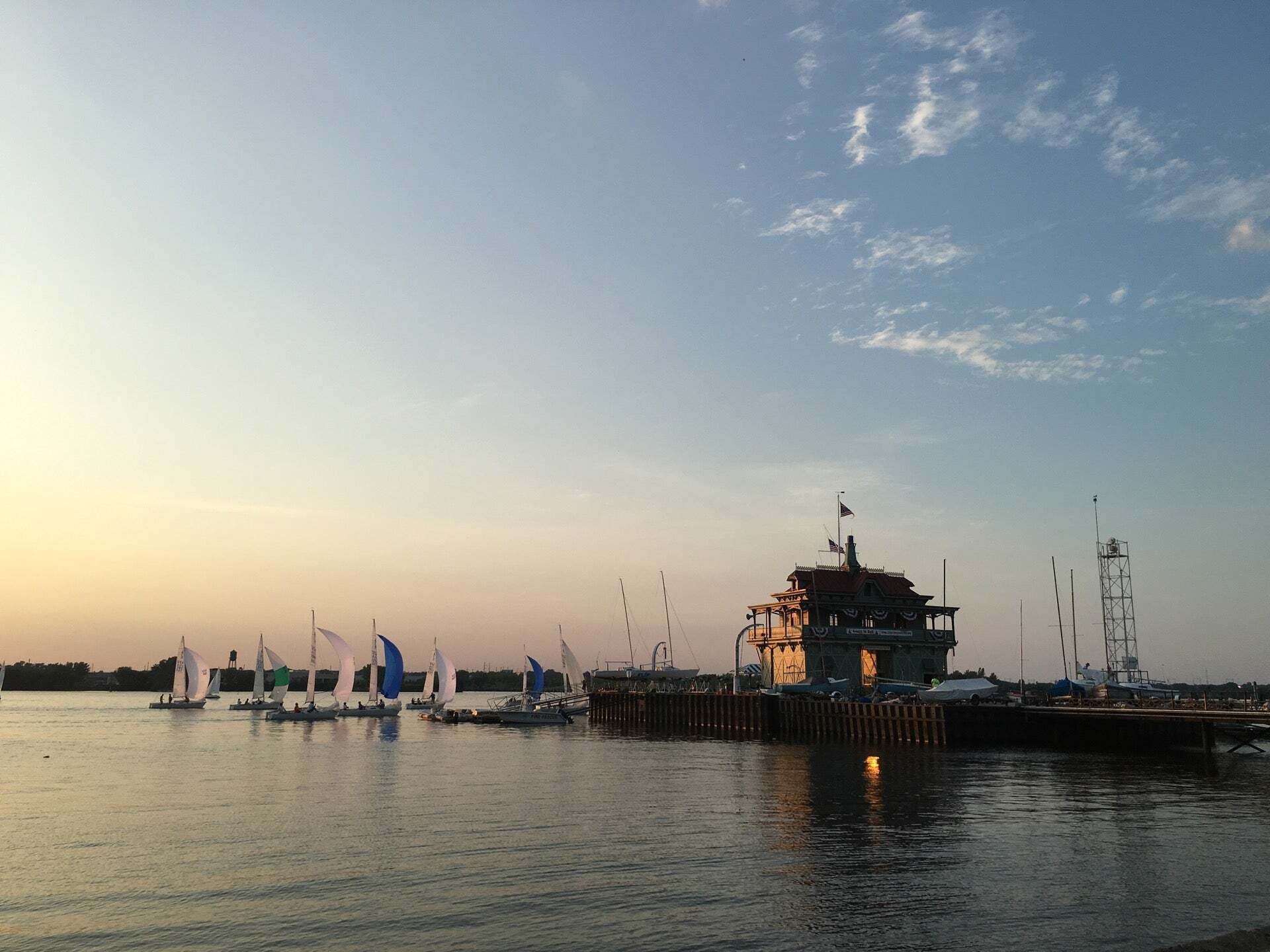 Sunset over a calm marina with sailboats and a lit pier against a pastel sky