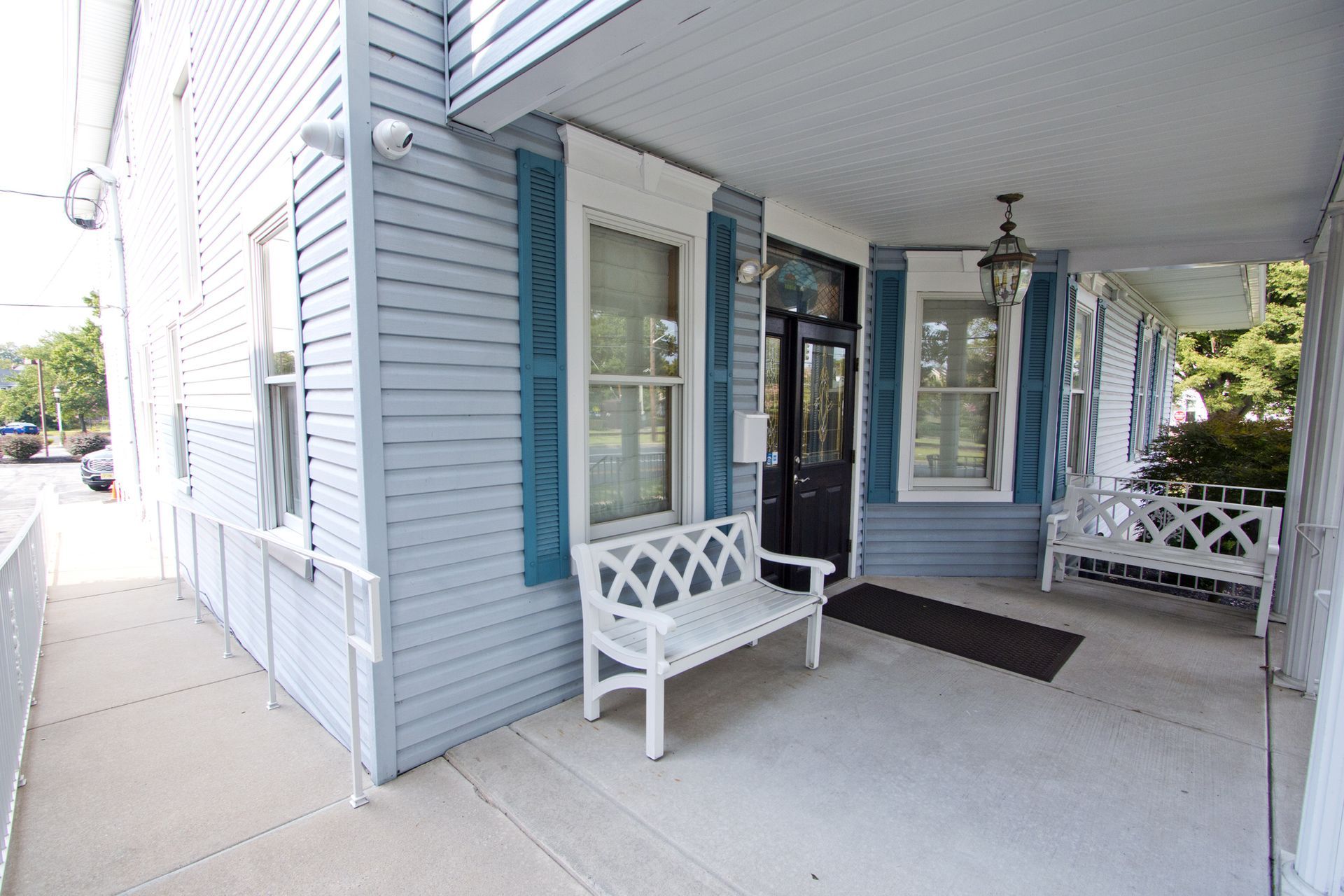 Covered front porch with white benches, blue siding, and a black door.