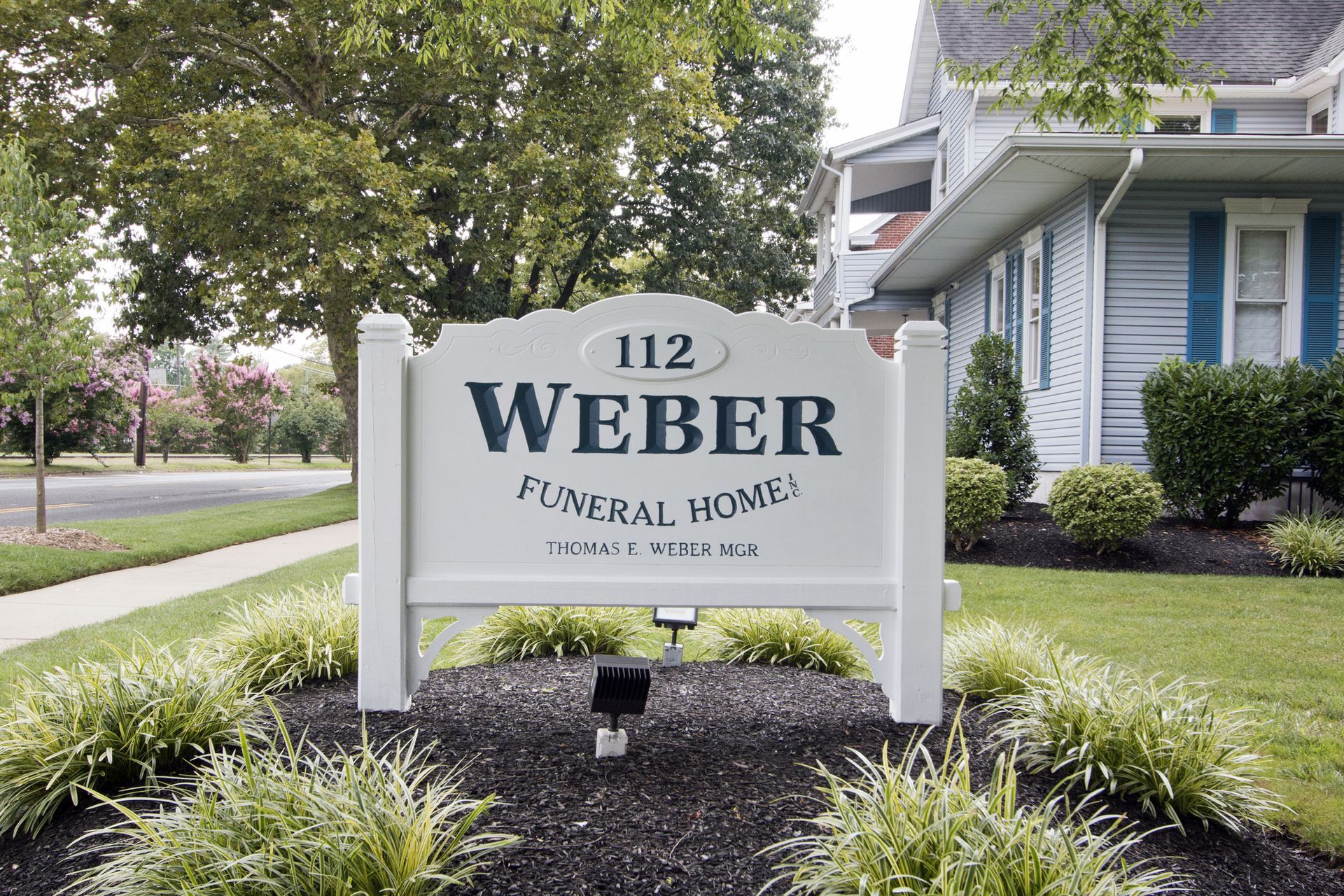 Weber Funeral Home sign in a landscaped suburban setting with blue house in background