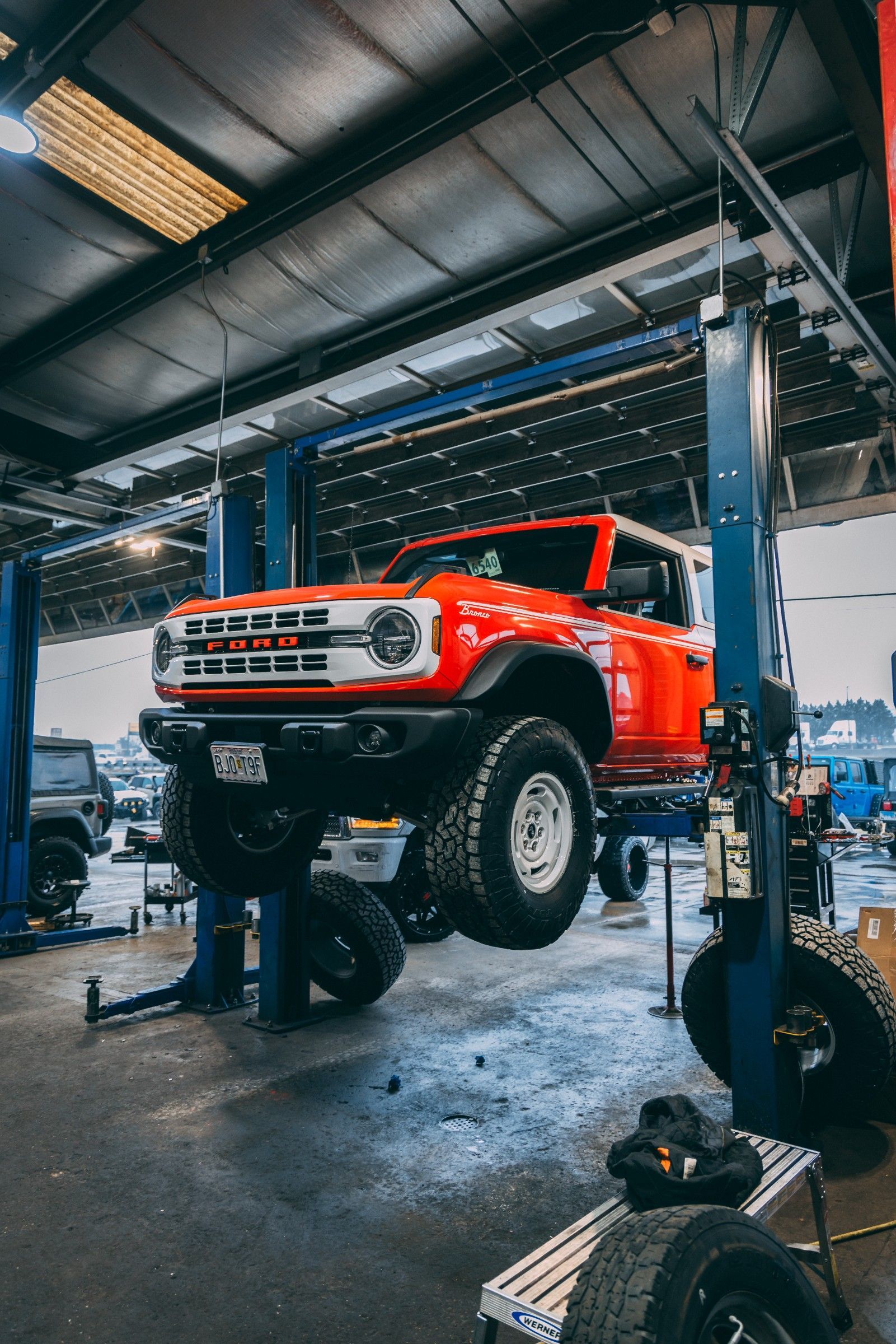 Orange ford truck up on mount in shop getting leveling kit installed