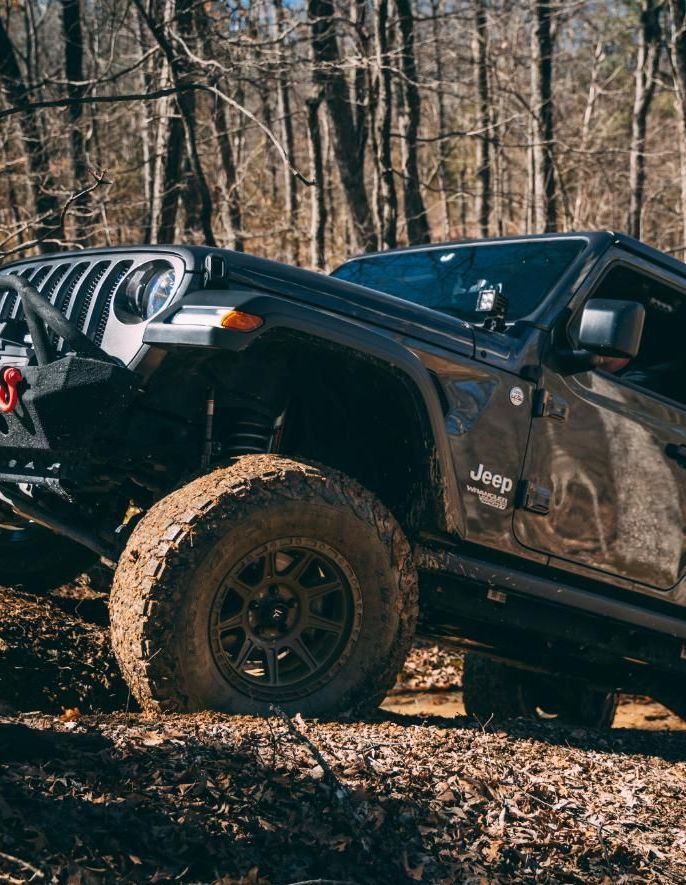 Dark Jeep off-roading in a muddy forest.