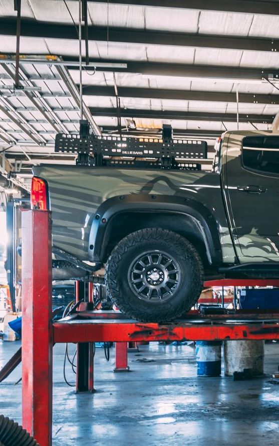 A gray truck on a red lift in a garage. The truck has a rack on the bed.