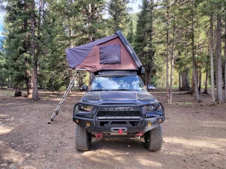 Black Toyota truck with rooftop tent in a forest setting.
