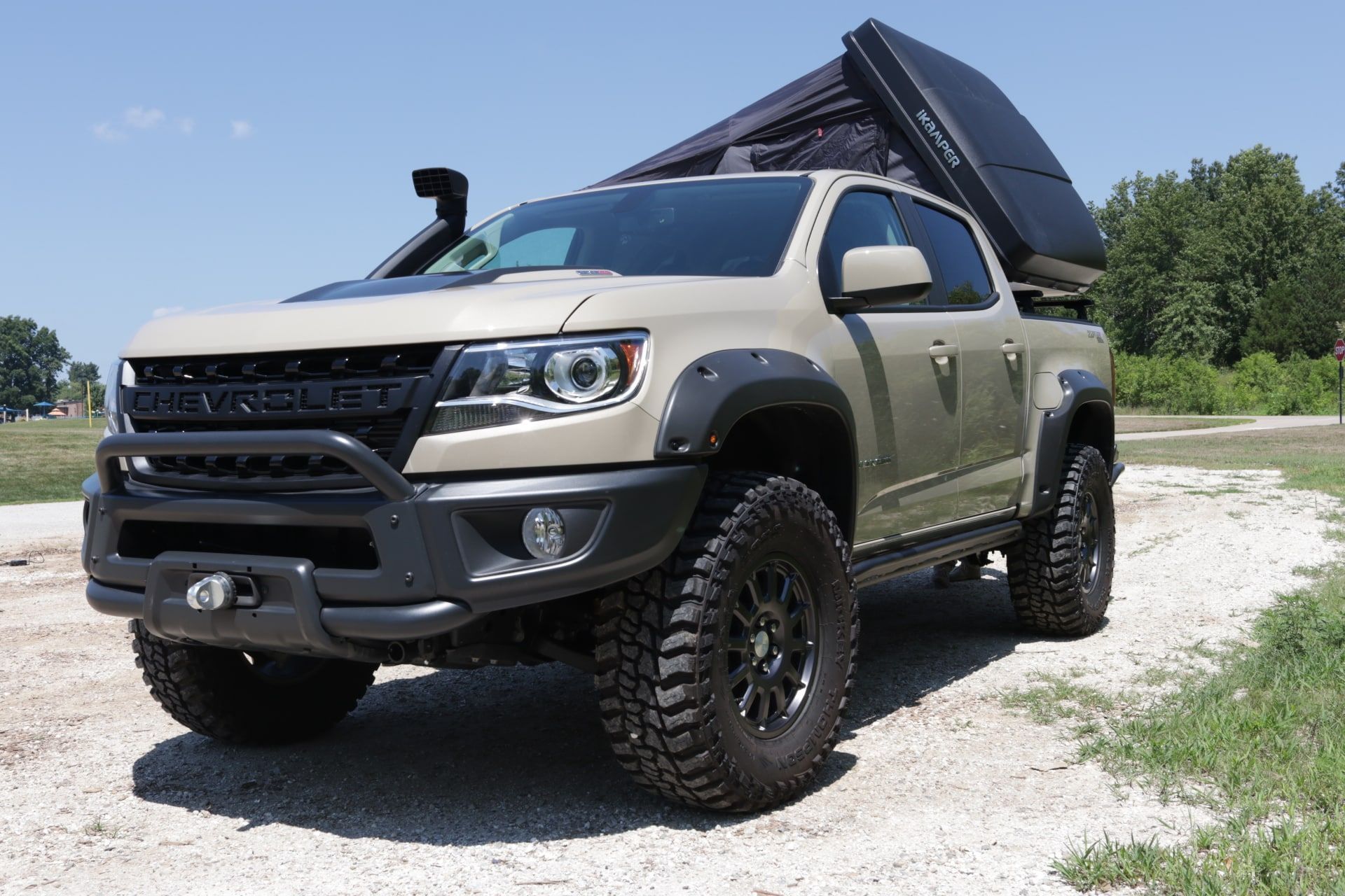 Tan Chevrolet Colorado pickup truck with a rooftop tent and off-road modifications.