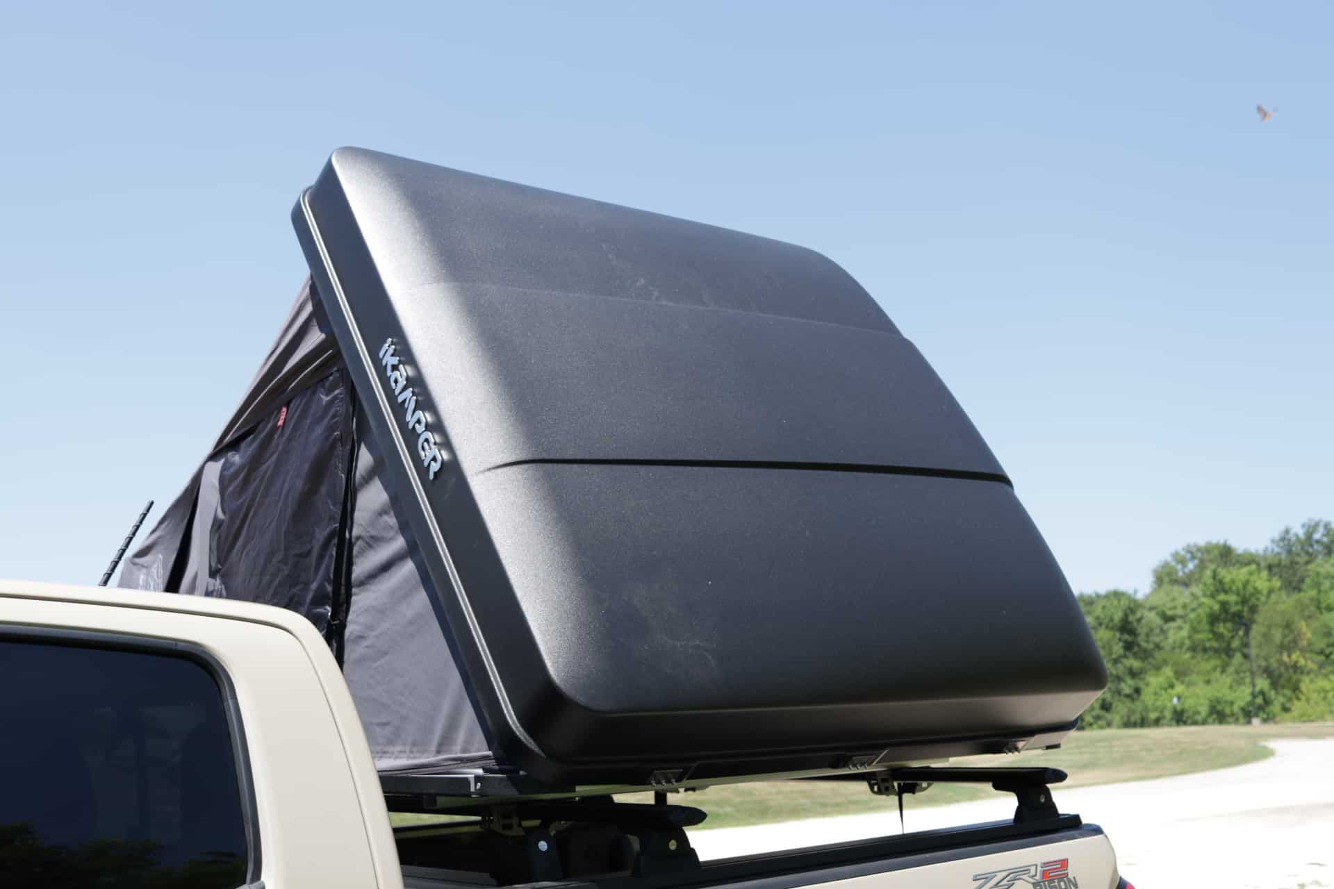 Black rooftop tent on a truck bed, open with tent fabric visible, set in a sunny, outdoor environment.