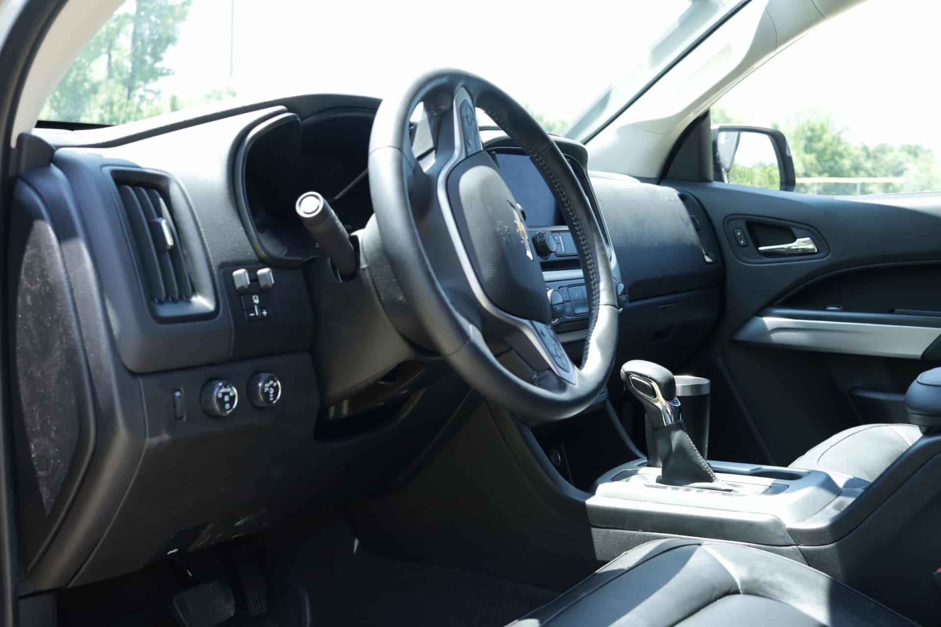 Black car interior with steering wheel, dashboard, gear shift, and touchscreen.