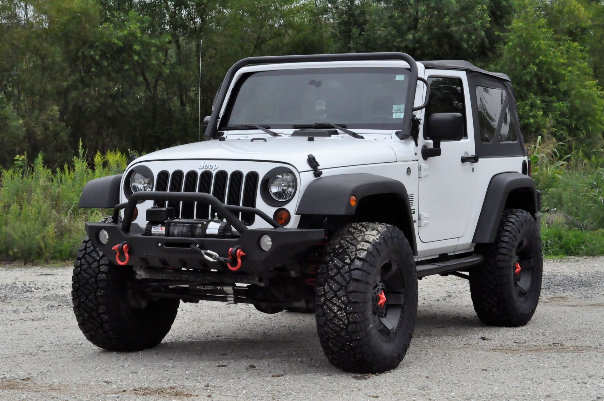 White Jeep Wrangler with black accents and off-road tires parked on gravel.