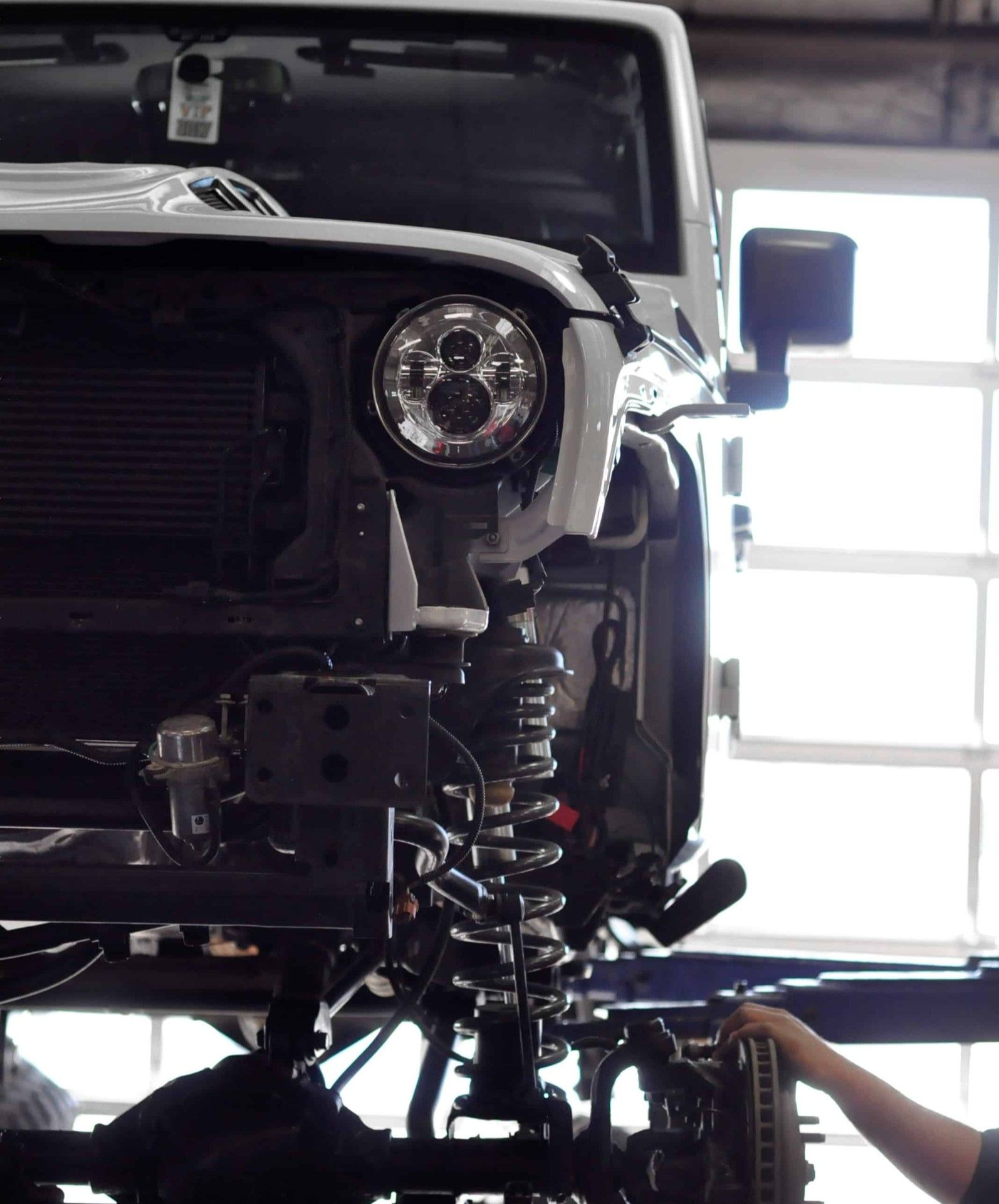 Close-up view of a white vehicle's front end mounted on a lift platform, showing a circular LED