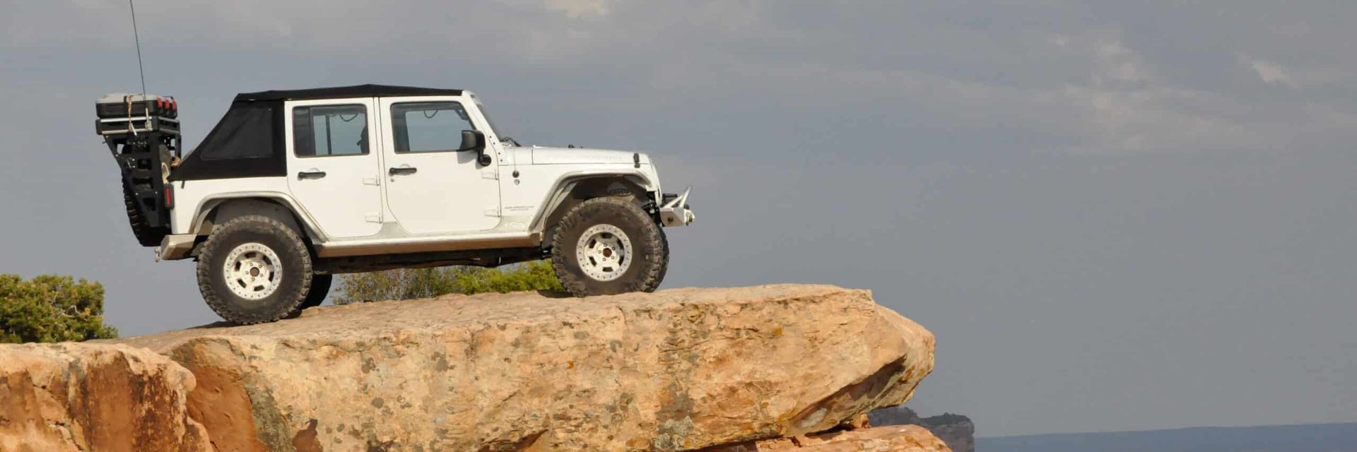 White Jeep at the edge of a cliff, against a cloudy sky.