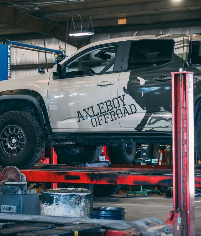 Off-road truck, white/gray camo, on a lift in a garage. 