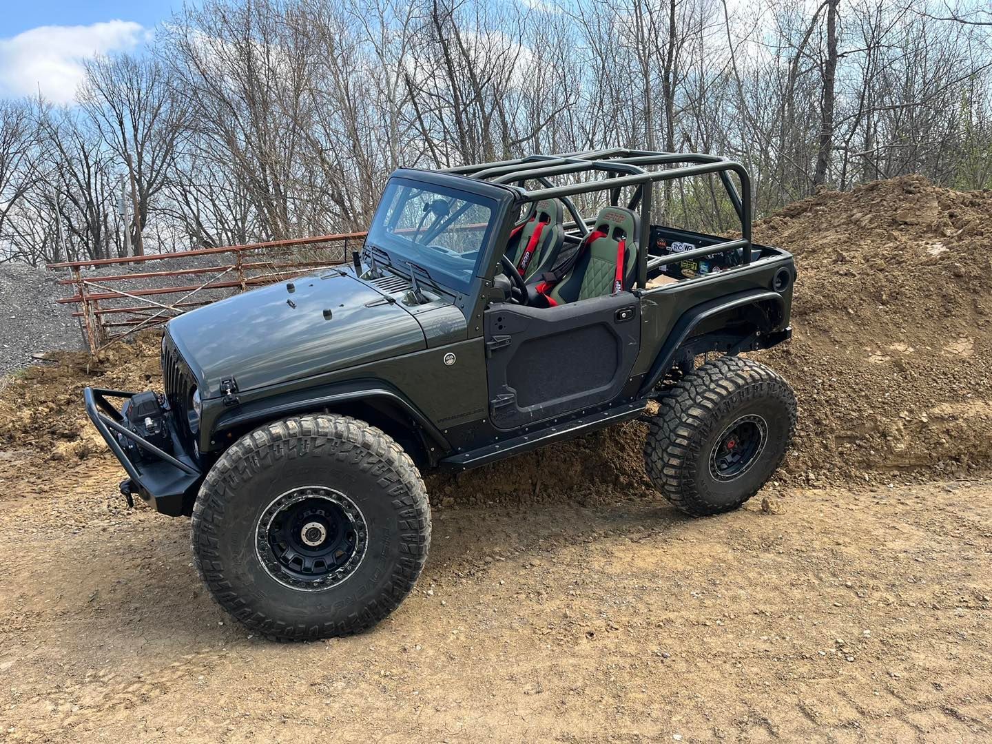 Dark green Jeep Wrangler with large tires off-roading on a dirt trail.