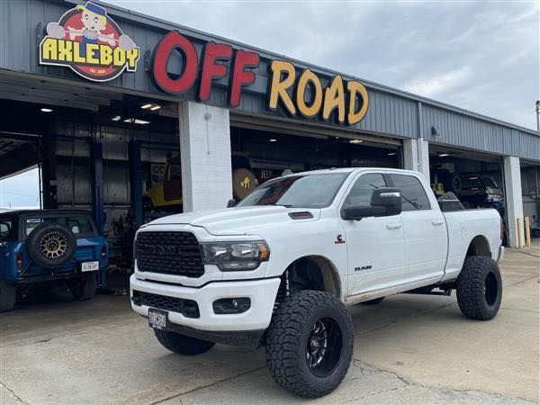 White lifted Dodge Ram truck parked in front of Axleboy Off Road shop.