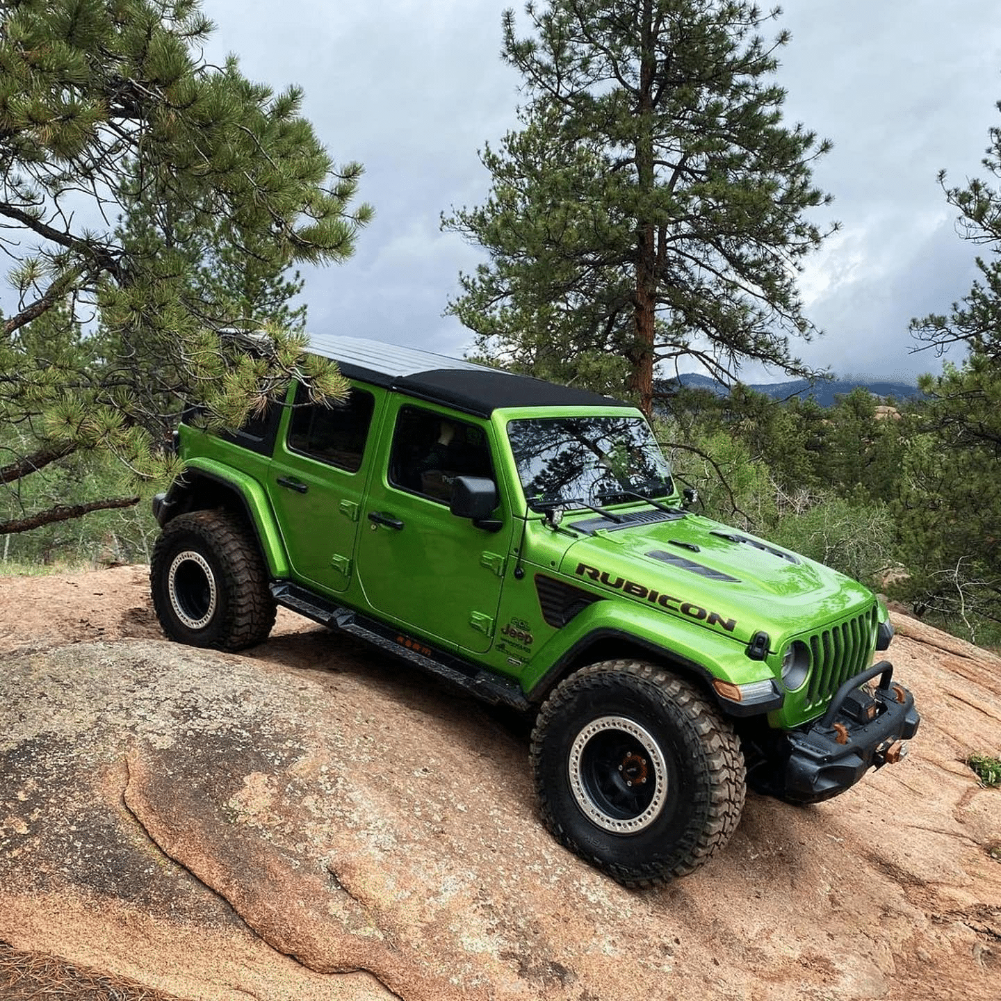 Green Jeep Wrangler Rubicon climbing a rocky hill in a forest.
